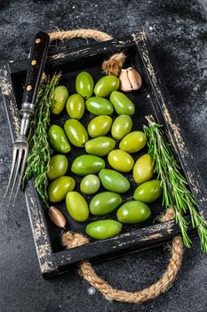 Fresh Green olives in wooden tray with thyme. Black background. Top view.