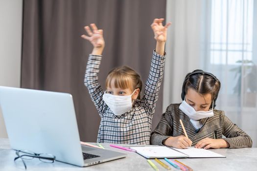 Distance Learning. School Girls At Laptop Wearing Mask Studying Online Sitting at the table at home