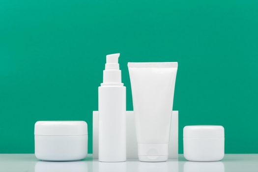 Set of white unbranded cosmetic bottles for daily skincare against dark green background. Concept of hygiene, man's skin care or anti acne treatment