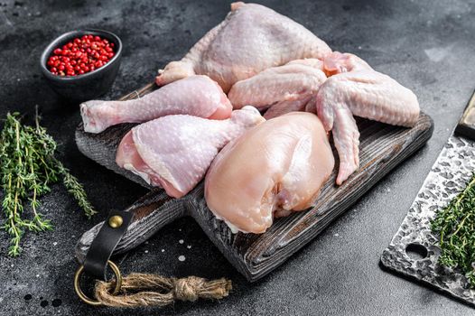 Raw chicken portions for cooking and barbecuing with skinless breasts, drumstick and wings. Black background. Top view.