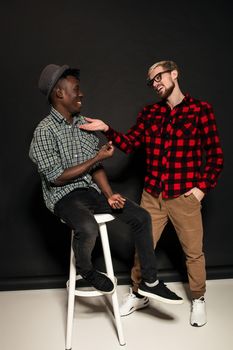 Studio lifestyle portrait of two best friends hipster boys going crazy and having great time together. On black background. Full-length photo