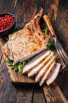 Grilled and sliced tomahawk pork chop meat steak on a marble board. Dark Wooden background. Top view.