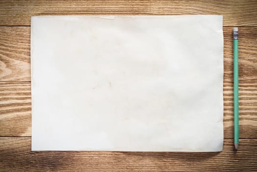 Sheet of paper lying on wooden table. Scrapbooking and hand made creativity. Rectangular blank white paper with pencil. Textured natural wooden background. View from above with copy space.