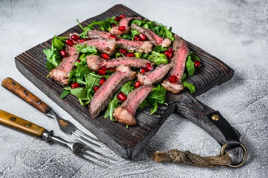 Sliced grilled beef steak with arugula leaves salad on rustic cutting board. White background. Top view.
