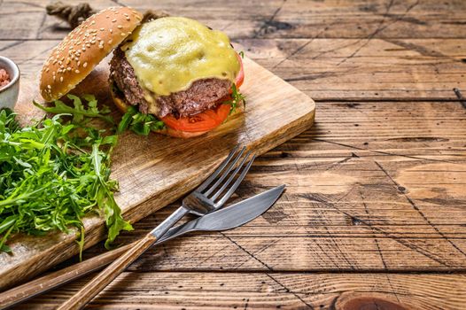 Big sandwich burger with beef, tomato, cheese and arugula. wooden background. Top view. Copy space.