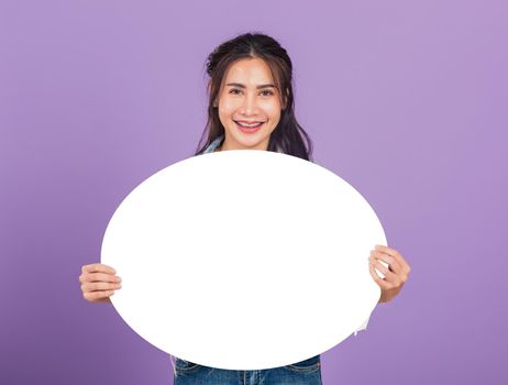 Happy Asian beautiful young woman smiling excited wear denims hold empty speech bubble sign, Portrait female posing show up for your idea looking at camera, studio shot isolated on purple background