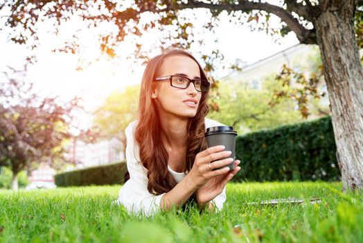 portrait of a young attractive woman in the park with a paper glass of coffee. Rest in the park