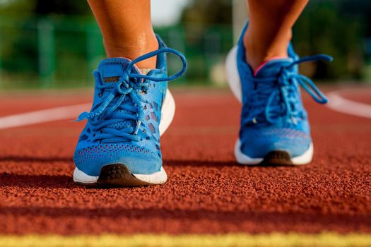 Close-up of woman's legs in blue sneakers on start before jogging. Red treadmill at the stadium