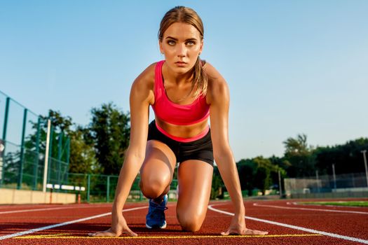 Young woman athlete at starting position ready to start a race. Female sprinter ready for sports exercise on racetrack.