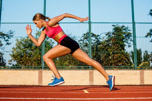 Runner sprinting towards success on run path running athletic track. Goal achievement concept. Female athlete sprinter doing a fast sprint for competition on red lane at an outdoor field stadium.