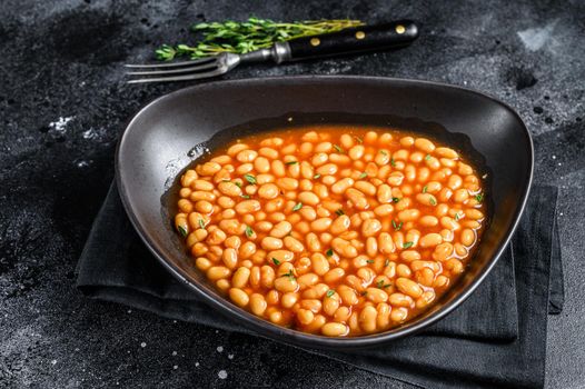 White beans in tomato sauce in a plate. Black background. top view.