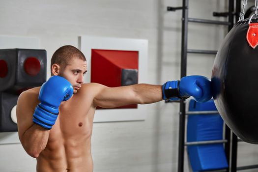boxer man during boxing hitting heavy bag at training fitness gym. naked torso
