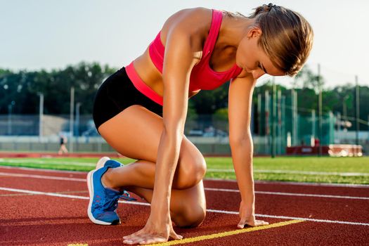 Young woman athlete at starting position ready to start a race. Female sprinter ready for sports exercise on racetrack.