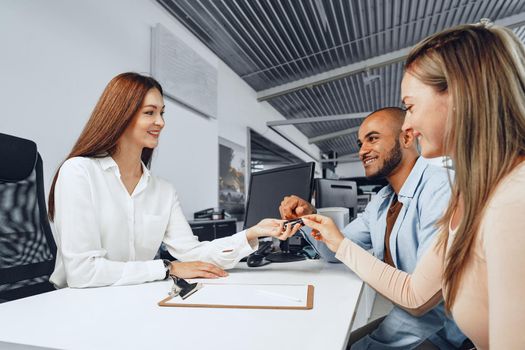 Cheerful couple taking keys of their new car in car dealership from saleswoman