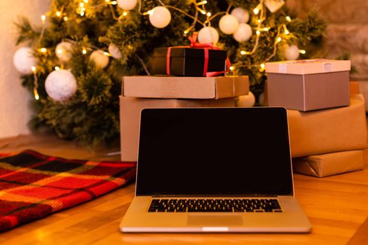 Laptop on the background of a Christmas tree accepts online congratulations merry christmas. Video call with the family in times of coronavirus.
