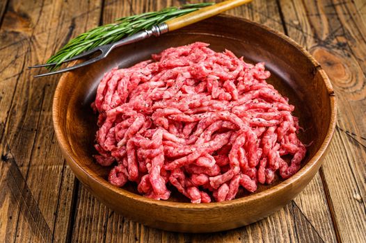 Raw mince lamb, ground mutton meat with herbs on a plate. Wooden background. Top view.