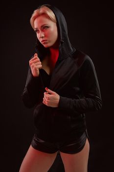 Beautiful seductive sporty girl with the slim sexy figure in the black hoodie, sport underwear and little black shorts is posing in the studio. Color filters.