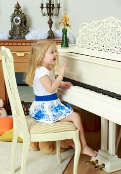 A little blonde is playing on a white grand piano.