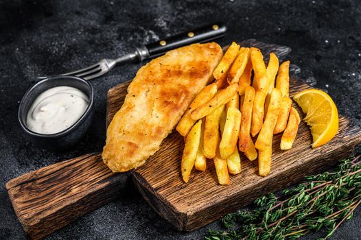 Fish and chips dish with french fries on wooden board. Black background. Top view.