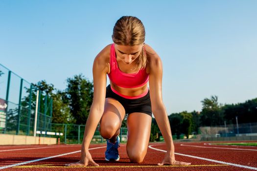 Young woman athlete at starting position ready to start a race. Female sprinter ready for sports exercise on racetrack.