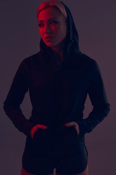 Beautiful seductive sporty girl with the slim sexy figure in the black hoodie, sport underwear and little black shorts is posing in the studio. olor filters.