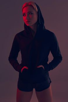 Beautiful seductive sporty girl with the slim sexy figure in the black hoodie, sport underwear and little black shorts is posing in the studio. color filters.