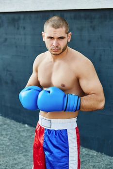 Boxer in multi-colored sports shorts and gloves practicing on the street. He looks into the camera.