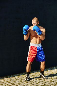 Boxer in multi-colored sports shorts and gloves practicing on the street.