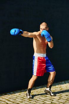 Boxer in multi-colored sports shorts and gloves practicing on the street.