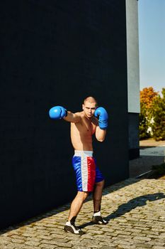 Boxer in multi-colored sports shorts and gloves practicing on the street.