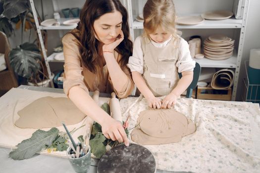 Woman and girl kneading clay. Family make art product at table in pottery workshop. Mother with daughter.