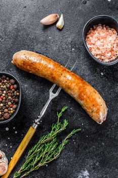 Pork Sausage bbg grilled with spices and herbs on a meat fork. Top view. Black background.