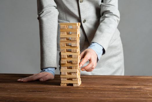 Businesswoman removing wooden block from tower on table. Management of risks concept with wooden jenga game. Business development and assistance. New challenge and leadership motivation.
