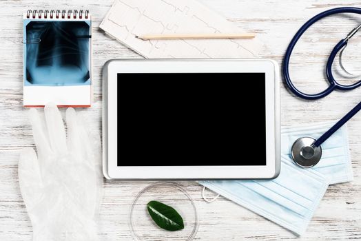 Mock up of doctors desktop with medical supplies. Tablet computer, x-ray image, stethoscope and cardiogram lies on wooden desk. Professional healthcare technology. Medical consultation and treatment.