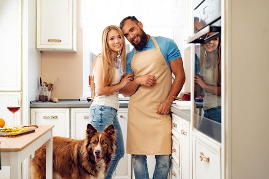 Happy smiling couple cooking food at kitchen with their dog