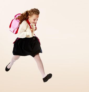 Pretty little girl schoolgirl in white blouse and black skirt to hurry to school. She jumps over the obstacle.On a brown gradient background.