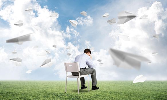 Businessman is sitting on an office chair with his head in his hands. Paper planes fly around