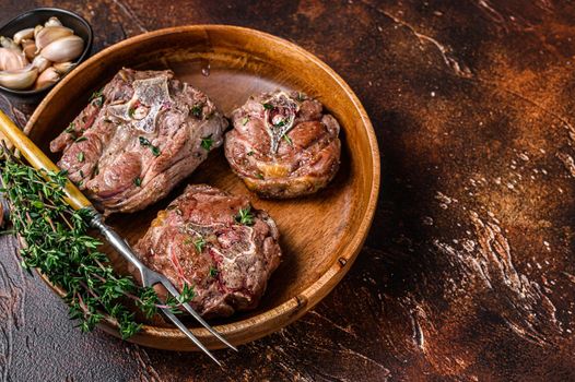 Fried lamb neck meat steaks in a wooden plate with herbs. Dark background. Top view. Copy space.