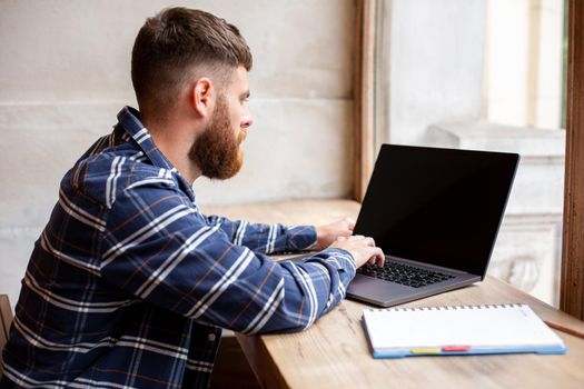 Young man chatting via net-book during work break in coffee shop, male sitting in front open laptop computer with blank copy space screen for your text message or advertising content