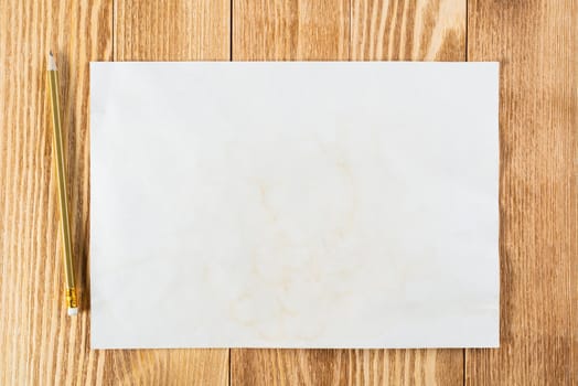 Sheet of paper lying on wooden table. Rectangular blank white old paper with pencil. Textured natural wooden background. Vintage copy space for design. Artist workplace and hand drawn skills