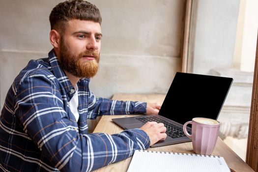 Young man chatting via net-book during work break in coffee shop, male sitting in front open laptop computer with blank copy space screen for your text message or advertising content