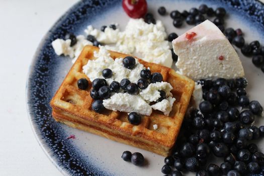 delicious healthy breakfast. Belgian soft waffles with curd cheese cream and blueberry cherries lie white blue plate view from the top. Delicious still life.