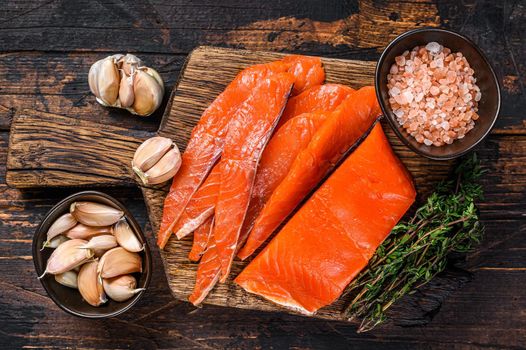 Sliced Smoked salmon fillet on a wooden cutting board with herbs. Dark wooden background. Top view.