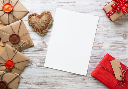 Flat lay composition with handmade fabric heart and gift box. Blank sheet of white paper on wooden surface. Romantic Saint Valentine's day congratulation. Merry Christmas and Happy New Year.