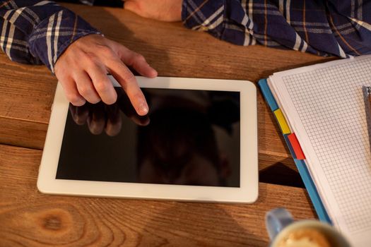 Cropped image of man using tablet works. White tablet with blank screen in a man hands on table at coffee shop or home office, working from cafe concept