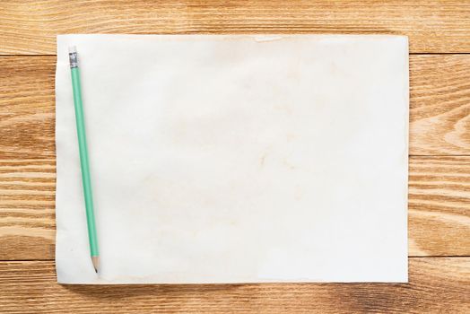 Business workspace with sheet of paper and pencil lying on wood table. View from above with copy space. Rectangular blank white paper on textured natural wooden background. Business presentation