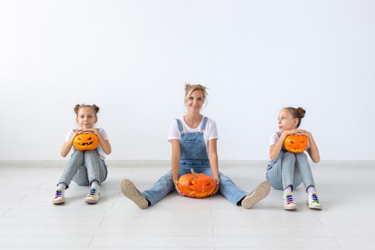 Happy halloween and holidays concept - A mother and her daughters with pumpkins. Happy family preparing for Halloween