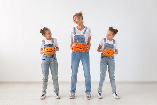 Happy halloween and holidays concept - A mother and her daughters with pumpkins. Happy family preparing for Halloween