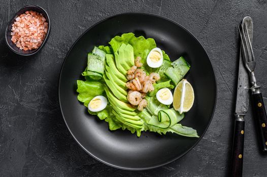 Fresh seafood salad with grilled shrimps prawns, egg, avocado and cucumber in a plate. Black background. top view.