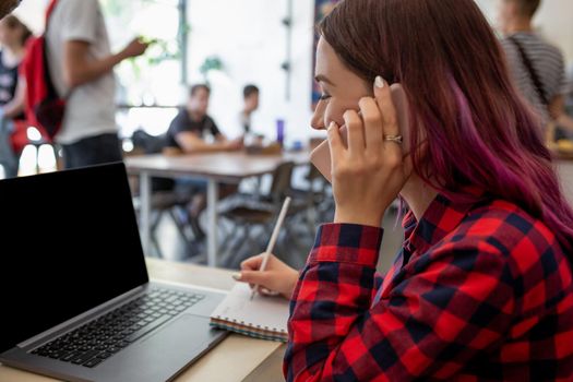 Rear shot of female student learning online via laptop before her lectures. Woman typing on notebook with blank screen with copy space for your text or advertising content, sitting at wooden table